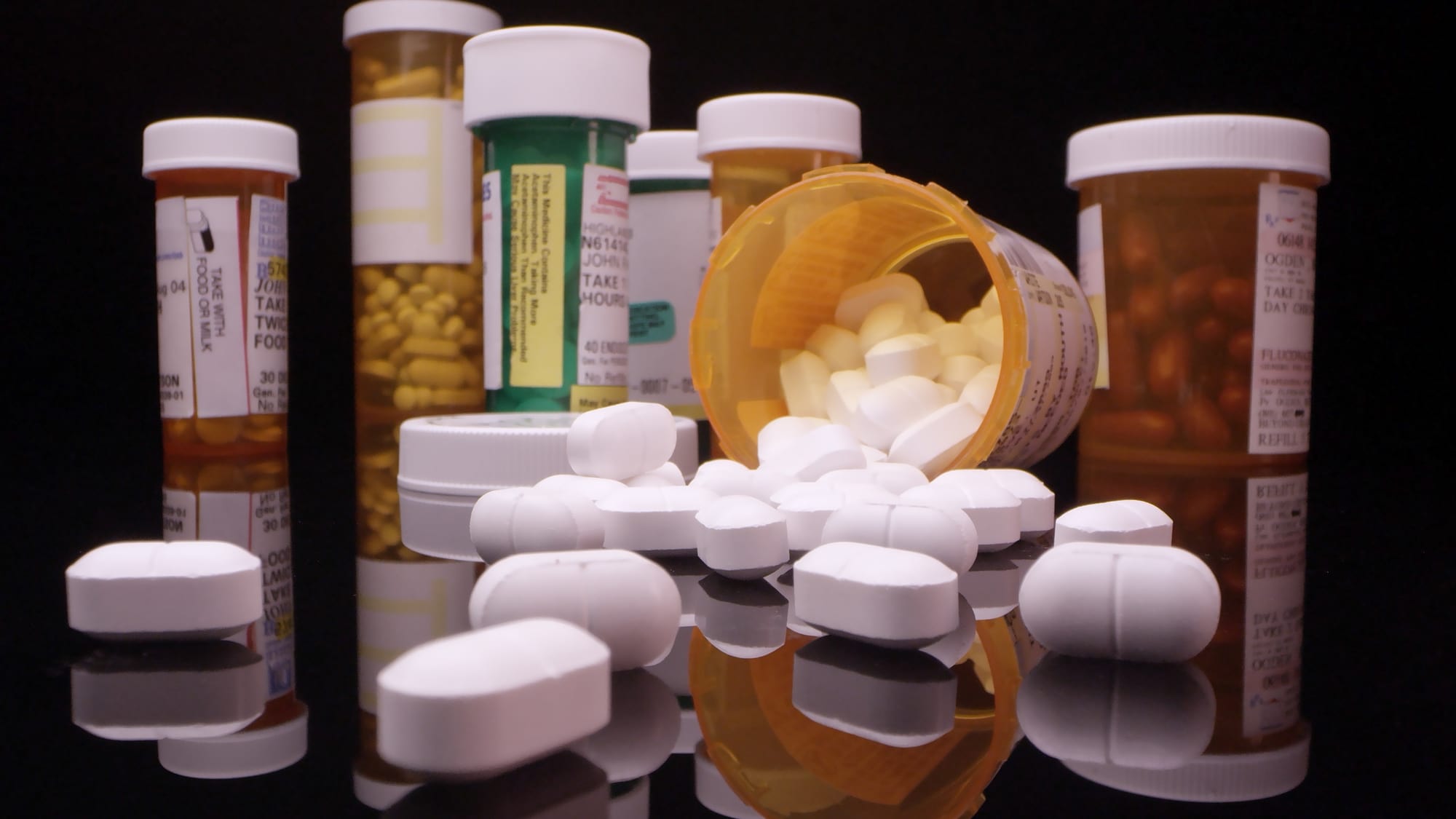 Numerous bottles of pills, some white pills scattered all over 