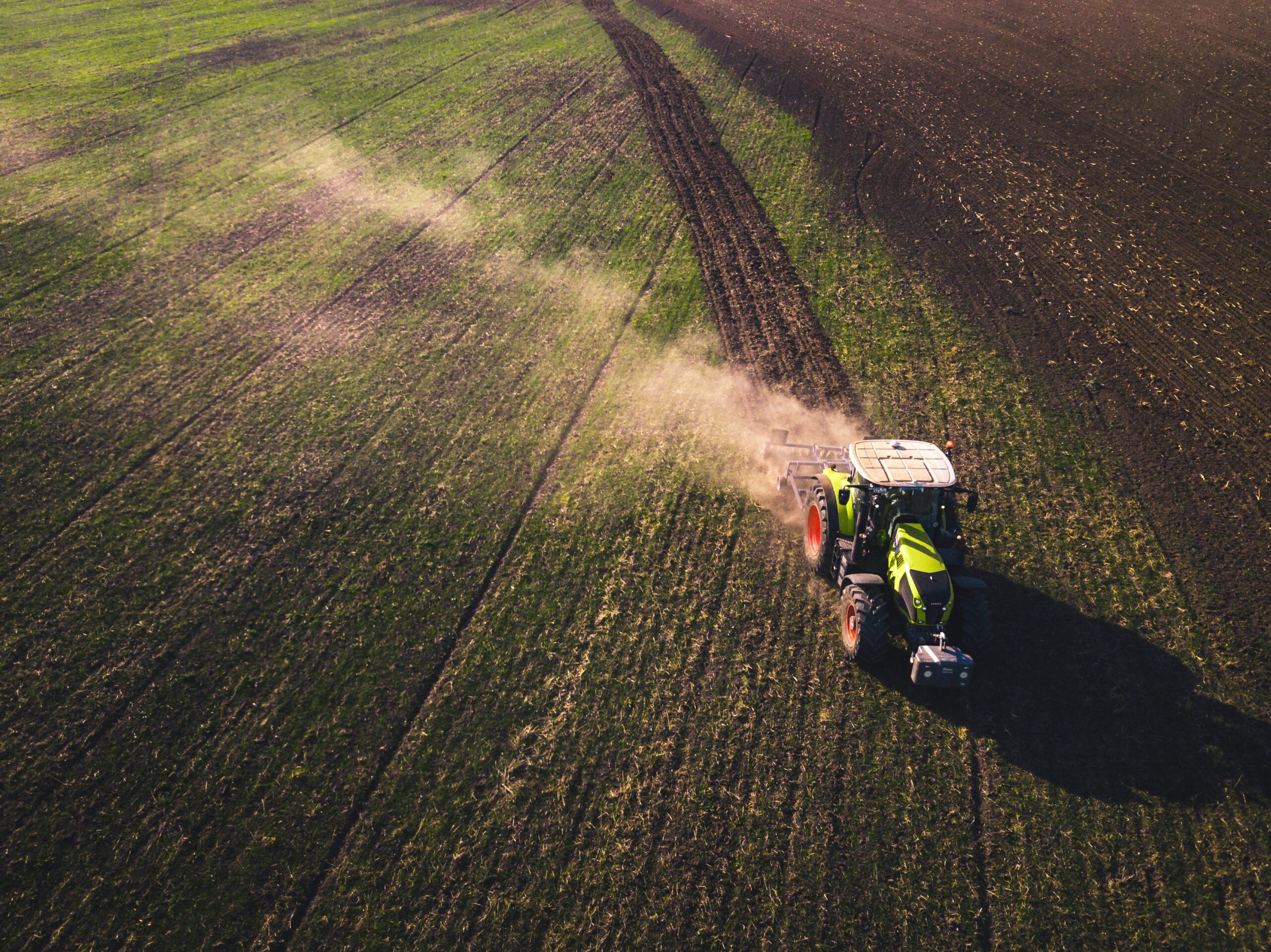 Aerial view of a tractor applying fertilizer across a vast agricultural field, showcasing modern farming practices