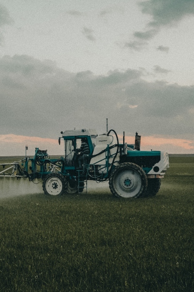 A tractor equipped with a sprayer applies chemicals to a vast green field under a clear blue sky